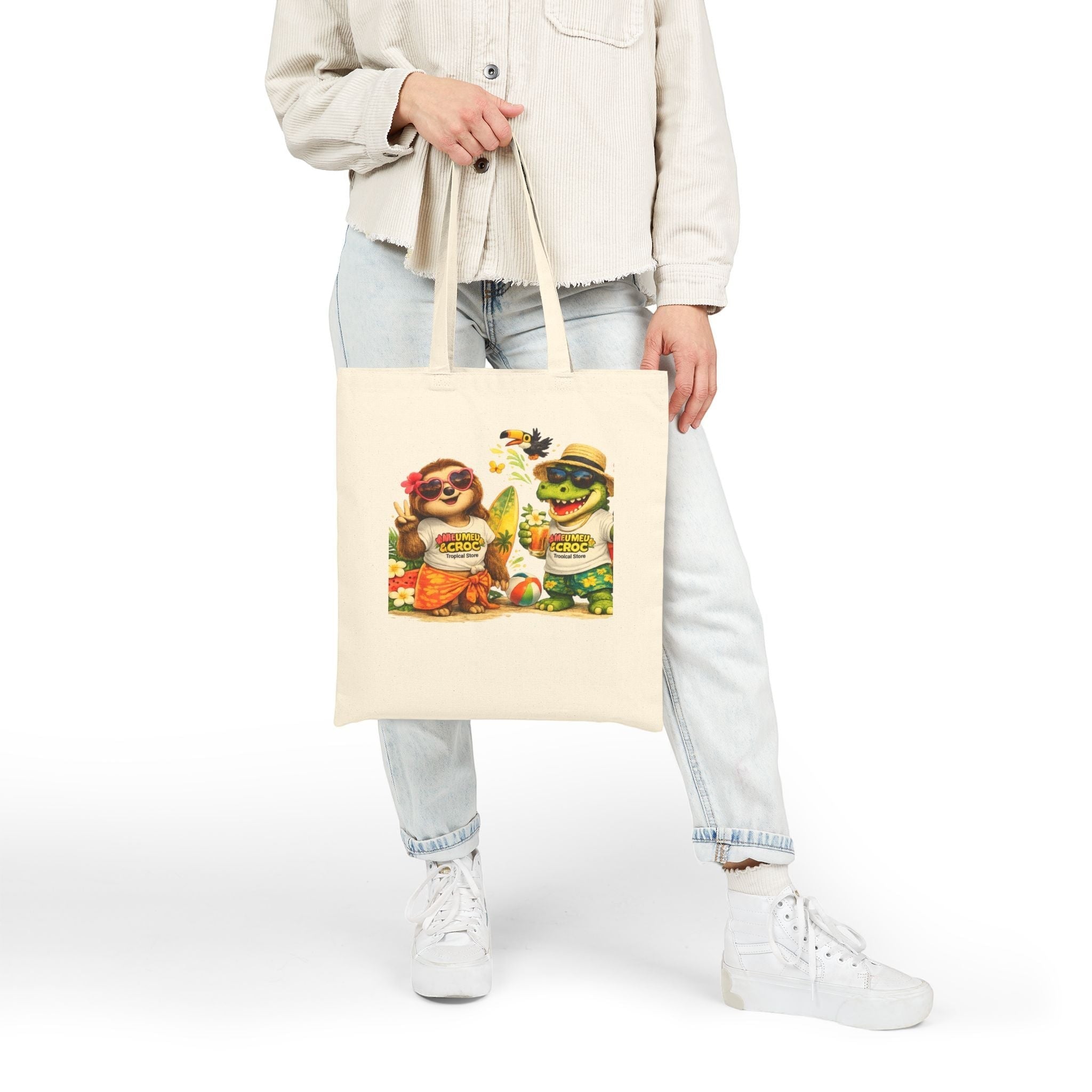 Meu Meu & Croc Tropical Store natural canvas tote bag with sloth and crocodile beach graphic held by a person.